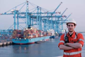 Offshore technician. Seafarer. Seaman. Navigator. A man in a boiler suit is standing in front of the port. Seafarer in front of the container terminal. - obrazy, fototapety, plakaty