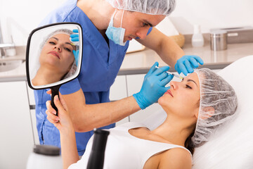 Young woman patient of beautician receiving rejuvenating facial injections, concept of aesthetic medicine
