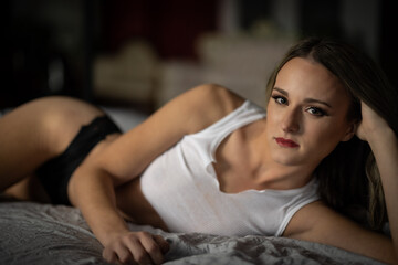 Blonde female in bed with a white tank top - obrazy, fototapety, plakaty