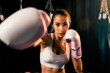 Asian female Muay Thai boxer punch fist in front of camera in ready to fight stance posing at gym...