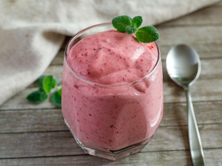 Healthy Strawberry or Raspberry Cream mousse in glass on a wooden table with mint leaves and spoon. Delisious summer dessert. Top view, close up