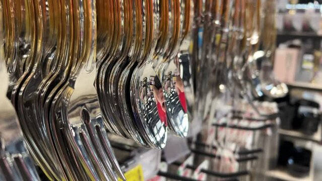 New cutlery - spoons and forks hanging on the counter in the crockery store or tableware shop. Close-up