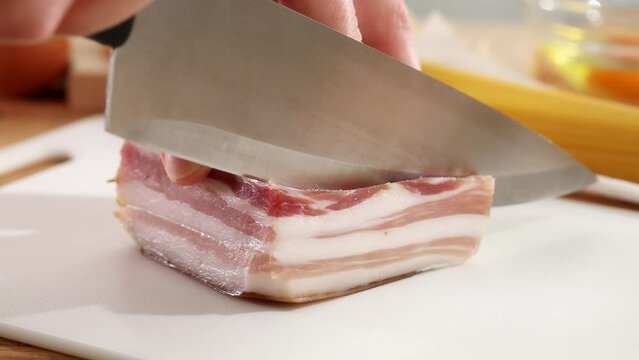 Cutting pancetta with a knife on a cutting board. Ingredient for pasta carbonara. Cooking traditional Italian food. High quality 4k footage