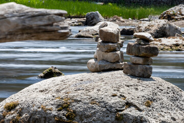 Fototapeta na wymiar Two inukshuks stand proudly on a boulder as they watch the milky waters from Sauble Falls pass them by.