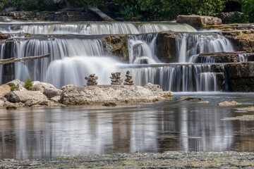 Three inukshuks stand in front of the milky waters of Sauble Falls at the south end of the Bruce Peninsula as they cascade over the rocks into the river.