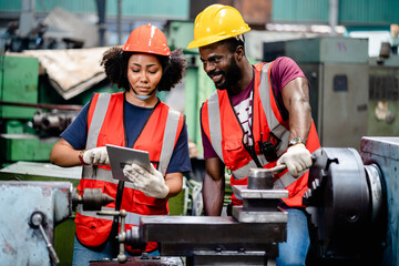 Two African American Mechanical Engineers using a digital tablet and discussing workshop machine...