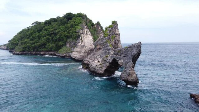 Natural arch Rock formation and limestone sea mount against Atuh Beach, Nusa Penida Island formed by Coastal erosion and Waves pounding on Karst cliffs. Aerial