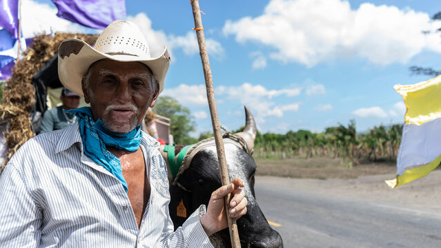 An elderly Latino man with hat and vitiligo being transported in a cart on a road