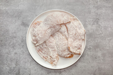 Top view of thin pieces of seasoned chicken breast coated with all purpose flour to make chicken piccata.