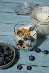 Morning granola breakfast with homemade greek yogurt, blueberries in glasses on blue wooden background. Healthy diet Crunchy granola with yogurt nuts and blueberries for healthy light breakfast