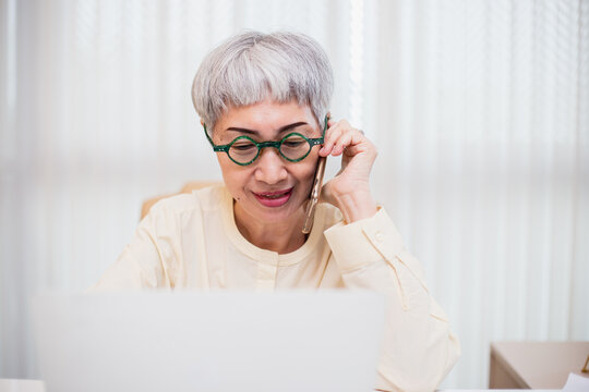 working in retirement concept, Asian senior business woman grey hair calling telephone sitting at office table. asian female senior cellphone smiling cheerful. middle aged female using phone.