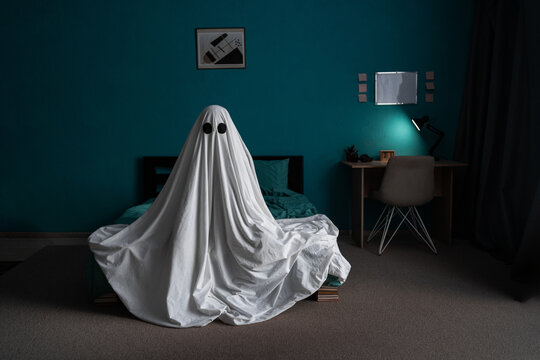 White ghost sitting on bed in bedroom, halloween concept.