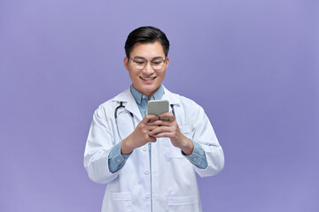 man doctor standing isolated on white background looking attentively at screen of cellphone,...