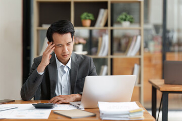 Financier a asian man feel stress with works, uses a laptop, makes a report to a finance company. Accounting and financial concept