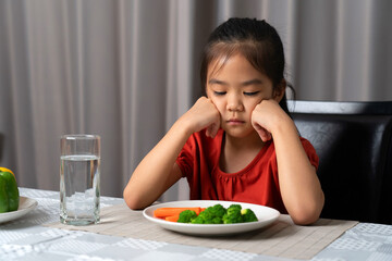 Little cute kid girl refusing to eat healthy vegetables. Children do not like to eat vegetables. - obrazy, fototapety, plakaty