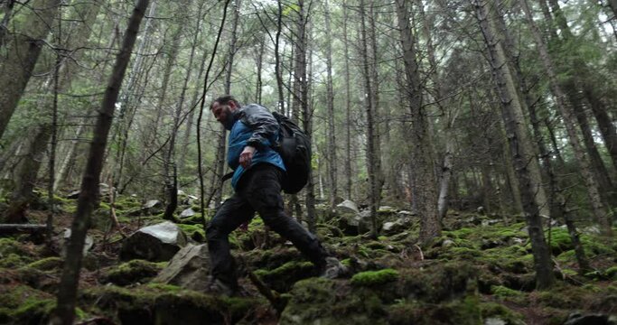 A young man in a mountain hiking with a backpack among the trees in a dense foggy forest. Single hike in long weather.
