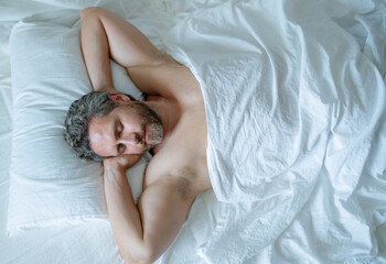 Man sleeping in bed. Top view of handsome man sleeping in bed. Morning healthy sleep. Guy sleeping on bed in bedroom. Middle aged adult man is sleeping at home. Cozy bed, white pillow mattress.