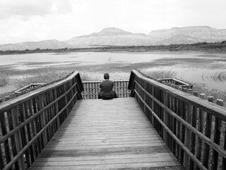 man sitting on wooden bridge over lake