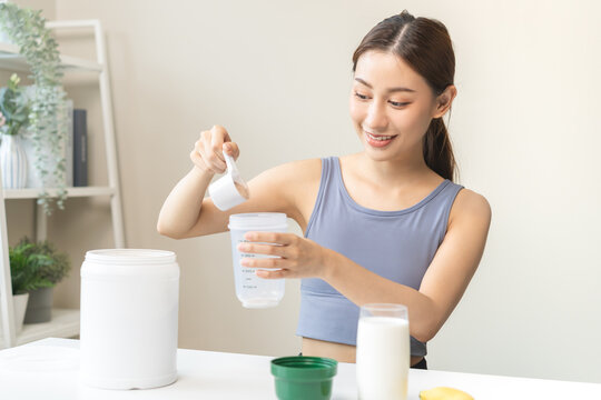 Diet meal replacement for weight loss, asian young woman in sportswear, hand in holding scoop making protein into bottle to shake, drink supplement for muscle after workout at home. Healthy body care.