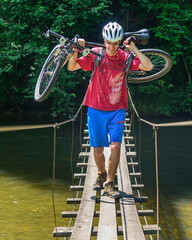 Mountainbiker trägt sein Rad über einen schmalen Steg am Fluß