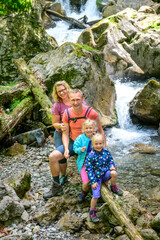 Fröhliche Familie posiert beim Wandern im Gebirge auf einem Baumstamm