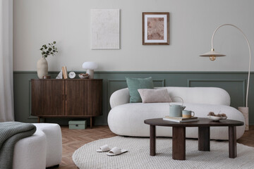 Warm and cozy living room interior with mock up poster frame, boucle sofa, wooden sideboard, coffee table, stylish lamp, gramophone, vase with leaves and personal accessories. Home decor. Template.