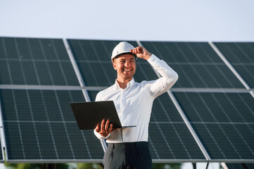Front view, holding laptop. Man is doing operating and maintenance in solar power plant