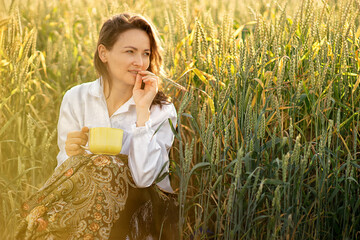 a young white woman went out at dawn to a wheat field to drink a cup of tea, she is sitting on the...