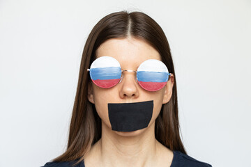 Russian flag on a girl's glasses and a mouth covered with a bandage on a white background, Russia's...