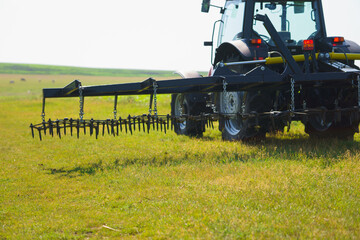 Red tractor with tooth harrow in the green field in Ukraine