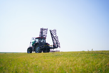 Red tractor with tooth harrow in the green field in Ukraine