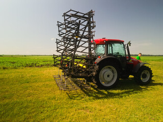 Red tractor with tooth harrow in the green field in Ukraine