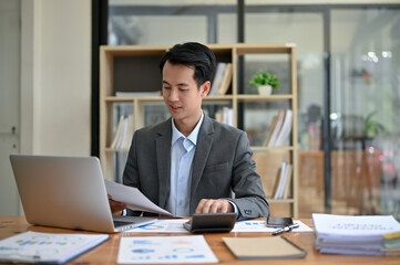 Obraz premium A professional Asian businessman focuses on business financial reports, working at his desk