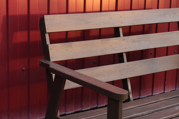 Wooden garden bench against the background of a fence made of red metal profiled sheet
