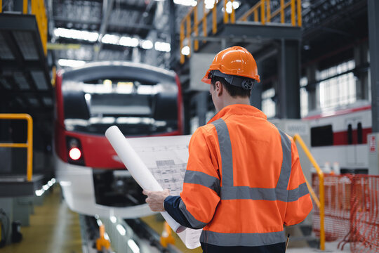 Electric train engineer mechanic staff worker with design plan for maintenance schedule check train running service in train factory workshop.