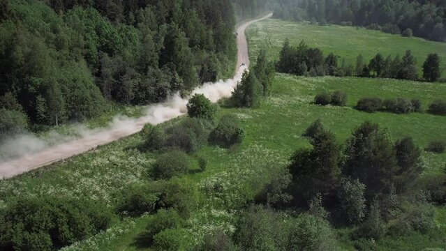 A rally car speeds along a road in a dense forest, kicking up dust. aerial photography