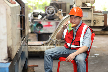 Asian technician engineer or worker man in protective uniform having lunch and eating sandwich and water at industry manufacturing factory