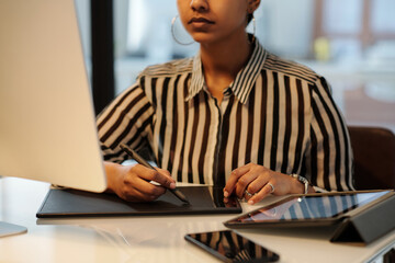 Hands of young female graphic designer with stylus and touchpad sitting by desk in front of...