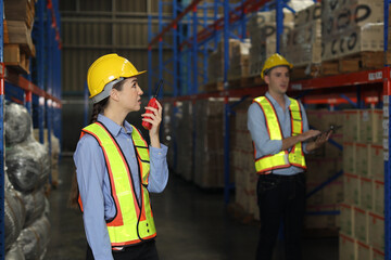 Group of warehouse workers with hardhats and reflective jackets using tablet, walkie talkie radio and cardboard while controlling stock and inventory in retail warehouse logistics, distribution center