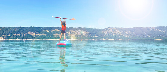 Child stands up paddle in lake- sport, adventure, family travel concept