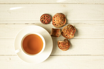 Cup of herbal tea and dried bael fruit on white wooden plate.