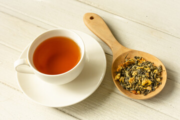 Cup of herbal tea and dried flower tea on white wooden plate.