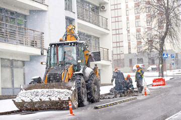 Tractor and construction worker team repair asphalt road during winter snow storm, pothole repair...