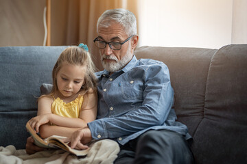 Granddaughter and grandfather looking serious as they read a book together