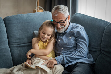 Little girl and grandfather smiling as he reads her a book	