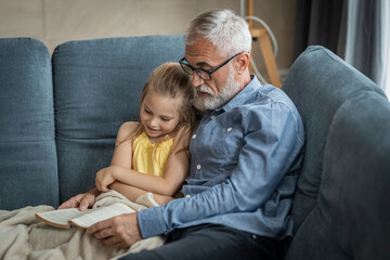 Obraz premium Little girl smiling as her grandfather reads her a book