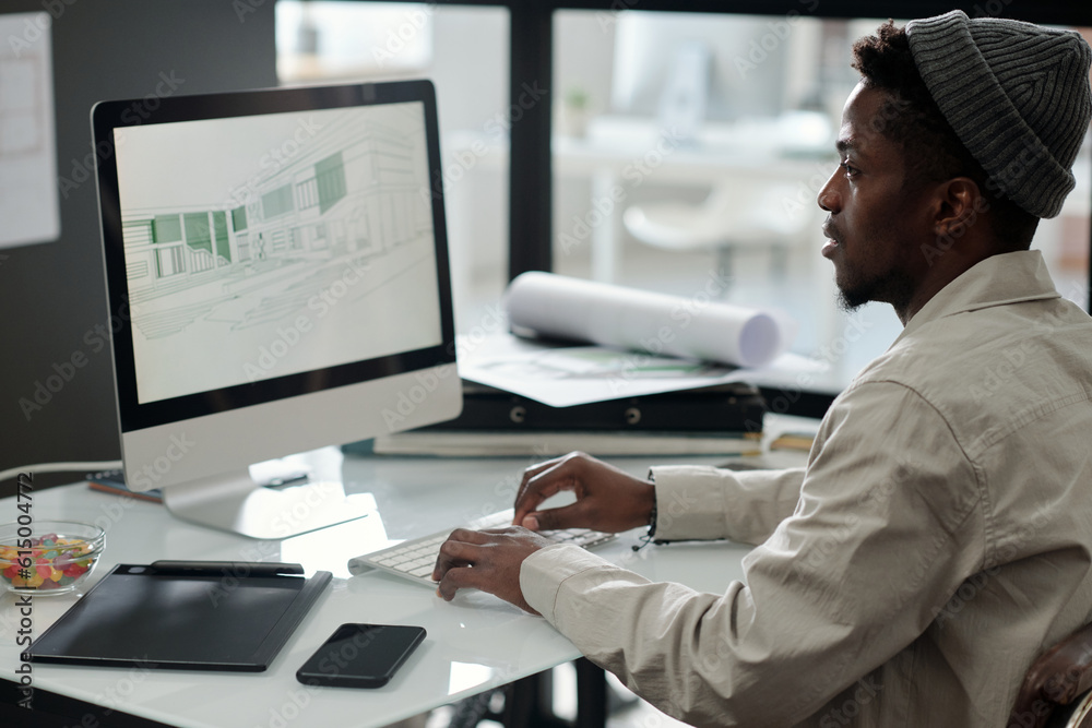 Aufkleber Young black man in casualwear looking at graphic sketches on computer screen while creating drawings for new architectural project