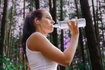 Fitness woman athlete drinking water after running at park.Thirsty sport runner resting taking a...