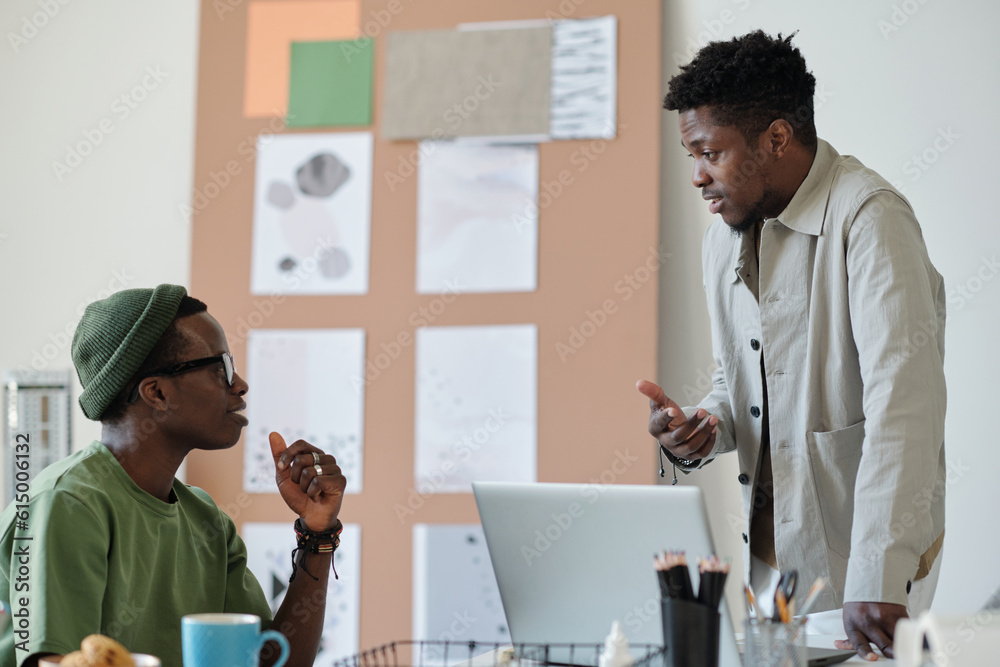 Poster Side view of two young African American designers discussing working points while one of them explaining something to colleague