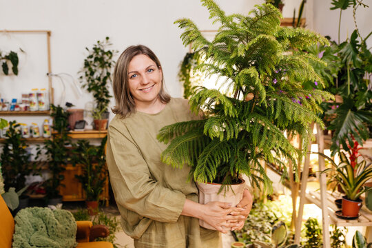 a woman stands in her home greenhouse holding a pot of araucaria